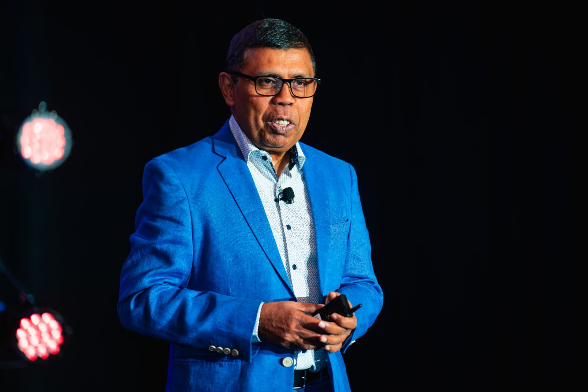 Arjun Sen presenting on stage, holding a remote, stage lights behind him